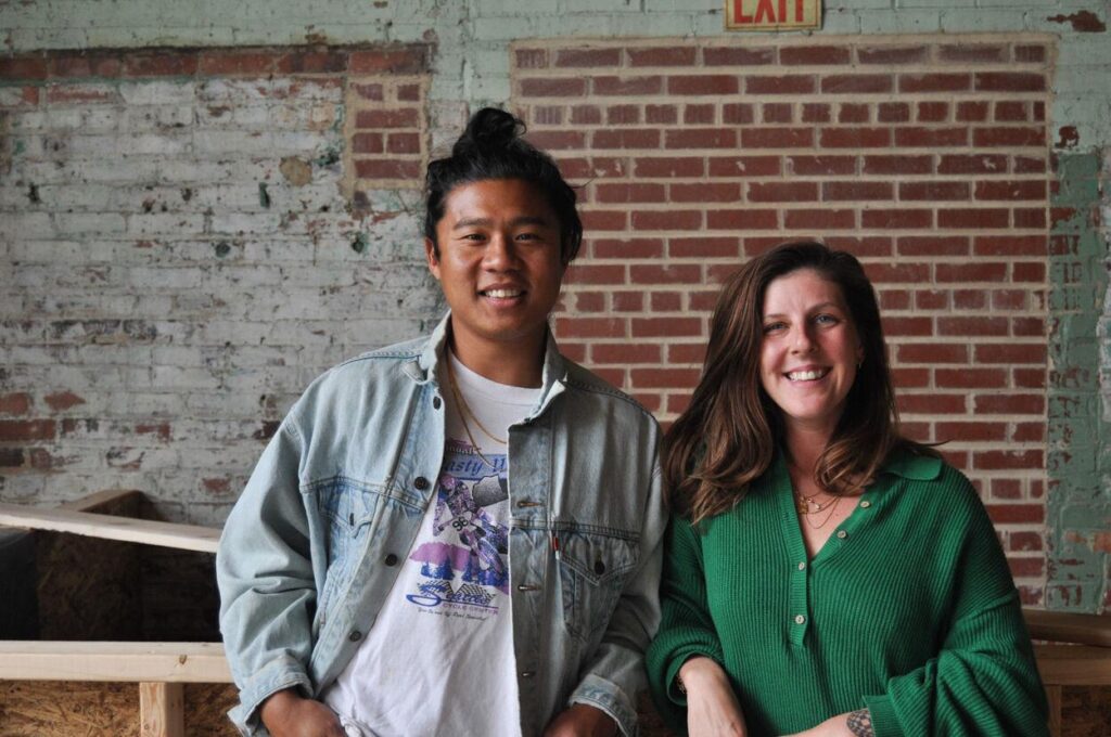 A couple standing in front of a brick wall smiling.